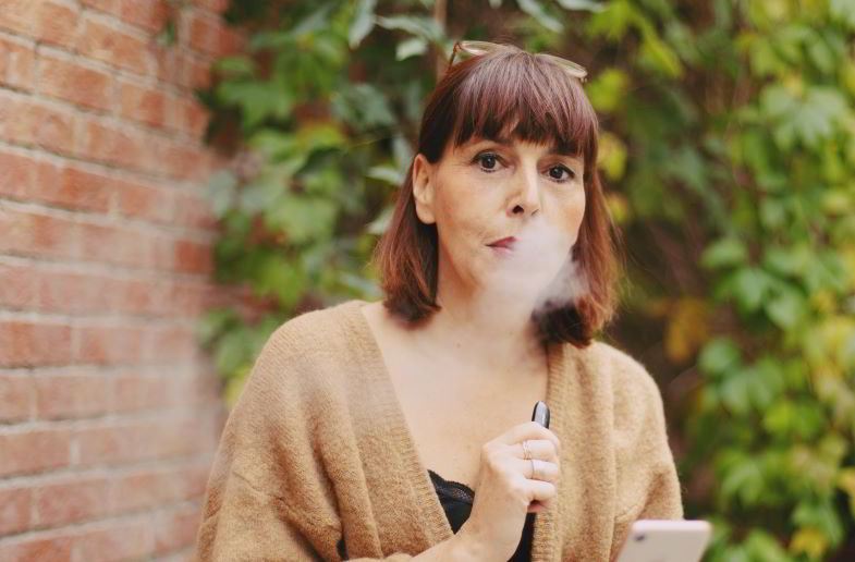 Mujer usando un cigarrillo electrónico en la mejilla